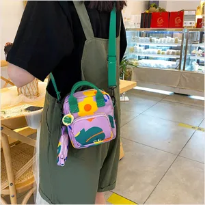 Detailed shot of a purple canvas crossbody bag with cute frog and flower print, green handle.