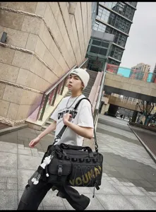 Detail view of large black travel duffel bag with shoulder strap in urban street style.