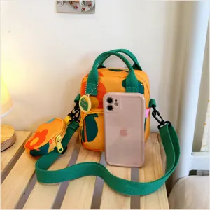Detail shot of yellow canvas crossbody bag with green straps and coin purse, size reference.