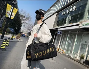 Detailaufnahme der großen schwarzen Reisetasche mit goldener Aufschrift und Tragegurt.