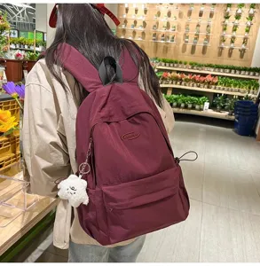 Detailed view of the casual solid color backpack with front pocket and cute plush pendant.
