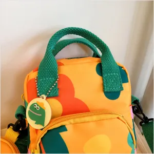 Close-up detail of the canvas crossbody bag, showing green handles and cute cartoon pendant.