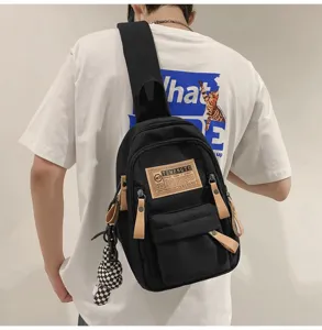 Detailed view of black canvas sling bag with leather patch and cute checkerboard charm.
