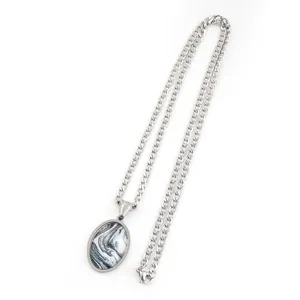 Gros plan détaillé d'un collier en chaîne métallique argentée avec pendentif ovale marbré.