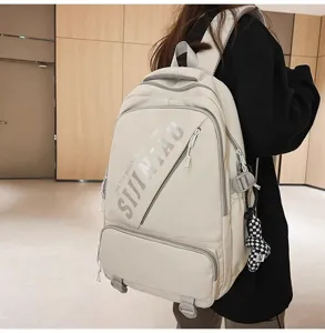 Detailansicht des trendigen, beigen Schulrucksacks mit Vordertasche und Karomotiv-Anhänger.