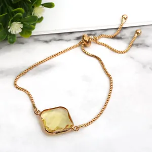 Gold-tone slider bracelet featuring a square yellow crystal pendant on marble background.