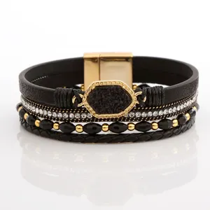 Nahaufnahme eines mehrlagigen schwarzen Lederarmbands mit Strasssteinen und Perlen.