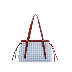 Detalle de bolso de hombro a cuadros azul y blanco con asas y correas de cuero rojo.