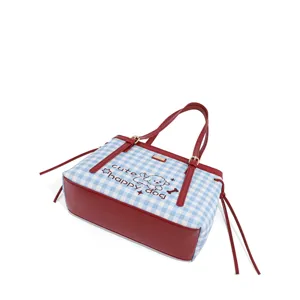 Detalle en primer plano del bolso tote de cuadros azul y blanco con ribete de cuero rojo.