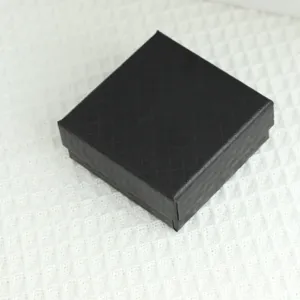Close-up van een zwarte vierkante sieradengeschenkdoos met diamantpatroon op witte stof.
