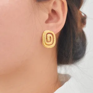 Close-up detail shot of elegant gold geometric spiral stainless steel stud earrings worn by model.