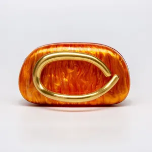 Amber acrylic evening clutch bag with striking sculptural gold metal ring handle.