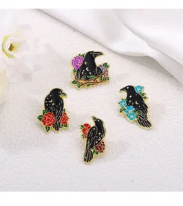 Close up view of dark gothic crow enamel pins with flowers and celestial star moon motifs.