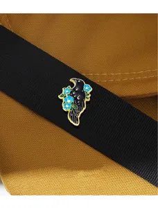 Close-up detail view of the creative dark style crow enamel pin with blue flowers and stars.