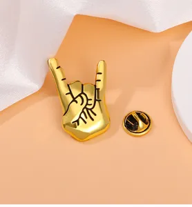 Gold metal rock hand gesture brooch detail view, stylish alloy lapel pin accessory.
