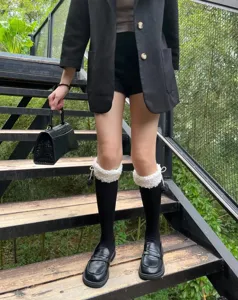 Detail view of black calf socks with white fluffy cuffs and pom poms worn on stairs.