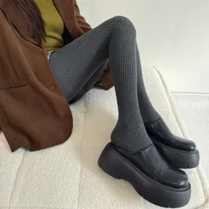 Detailed view of dark grey ribbed tights worn by model sitting on soft white cushion.