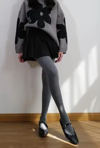 Dettaglio di collant a coste grigi indossati con maglione in maglia e gonna.
