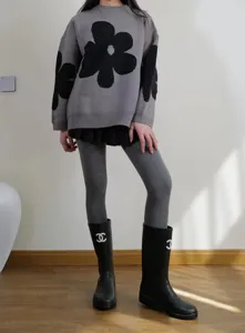 Primo piano di collant a coste grigi indossati con un maglione fantasia e stivali neri.