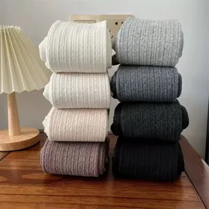 Detail shot of stacked thick ribbed tights in various colors like white, grey, and black.