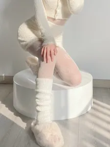 Close-up detail of cozy white knitted leg warmers and patterned tights paired with fluffy slippers.