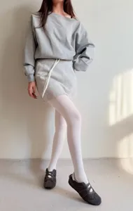Detailed shot of casual grey sweatshirt and skirt outfit paired with smooth white pantyhose.