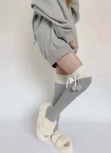 Gros plan sur les chaussettes hautes gris et blanc avec pompons mignons et nœud délicat.