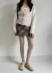 Close-up detail of stylish ribbed fleece-lined tights styled with plaid skirt and knit cardigan.