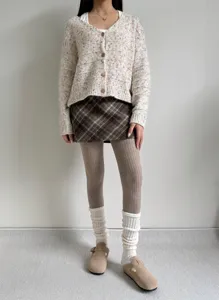 Detailed view of women's ribbed brown thermal tights styled with knit cardigan and skirt.