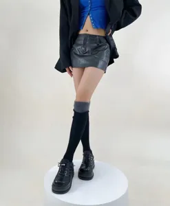 Détail de tenue de mode féminine élégante avec blazer noir, mini-jupe et chaussettes.