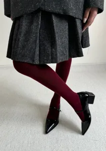 Gros plan détaillé d'une jupe plissée en laine, collants bordeaux et chaussures noires.