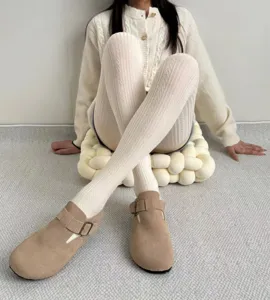 Detailed shot of textured cable knit tights worn with cozy neutral clogs in a clean room.
