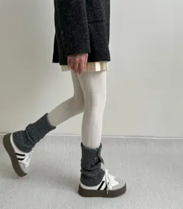 Vue détaillée de collants blancs en tricot torsadé associés à des jambières grises.