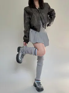 Dettaglio di scaldamuscoli in maglia grigia a righe, abbinati a scarpe in stile retrò.