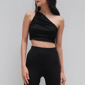 Close-up detail of stylish black one-shoulder pleated crop top, slim fit design texture.