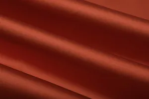 Red satin dress fabric detail showing smooth texture and elegant folds for fashion apparel.