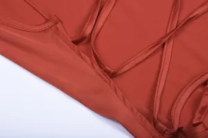 Detail shot of elegant women's satin slip dress with thin cross straps in rust red.