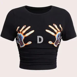 Nahaufnahme Detail des schwarzen kurzarm bauchfreien T-Shirts mit Strass Buchstabe D.