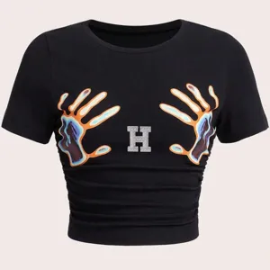 Nahaufnahme des schwarzen T-Shirts mit Strass-Buchstabe H und auffälligem Hand-Print.