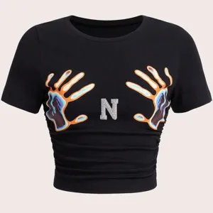 Nahaufnahme des schwarzen Kurzarm-Crop-T-Shirts, Hand-Grafikprint und Strass-Buchstabe N.