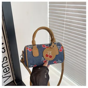 Blue denim cherry print barrel bag, stylish shoulder crossbody bag with brown handle.