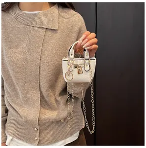Detailaufnahme einer kleinen weißen Handtasche mit edlem Metallschloss und feiner Kette.