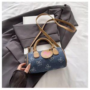 Detail shot of blue denim barrel bag featuring white bow print and brown leather handle.