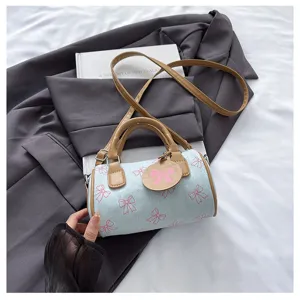 Close-up detail of blue denim barrel handbag featuring cute pink bow prints and brown handles.