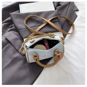 Detail view of the cute denim cylindrical handbag featuring pink bow prints and brown handles.