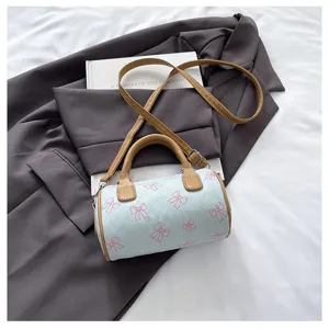 Close-up detail of cute cylindrical shoulder bag featuring bow print and brown leather handles.