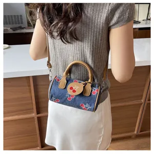 Detailed shot of a stylish denim cherry print barrel crossbody bag with brown handle and charm.