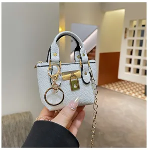 Weißes Mini-Handtaschen-Detail mit Gold-Schloss, Schlüsselanhänger und feiner Kette.