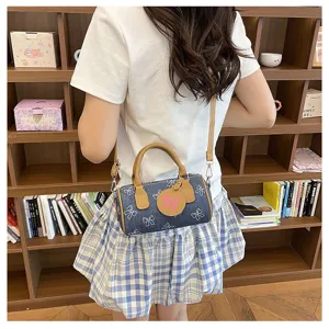 Stylish denim barrel shoulder bag with cute bow print and brown handle in daily wear view.