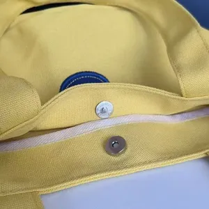 Close-up detail of the durable yellow canvas tote bag featuring a secure metal magnetic snap button.